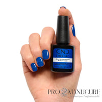 Main aux ongles bleu cobalt brillant tenant le flacon CND Shellac Blue Eyeshadow 12,5 ml