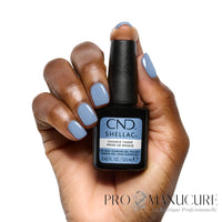 Main aux ongles bleu pastel brillant tenant le flacon CND Shellac Chance Taker 12,5 ml