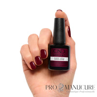Main aux ongles rouge cerise bordeaux brillant tenant le flacon CND Shellac Cherry Apple