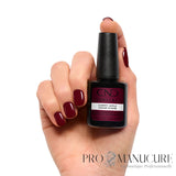 Main aux ongles rouge cerise bordeaux brillant tenant le flacon CND Shellac Cherry Apple