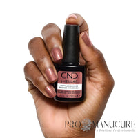 Main présentant une manucure bronze rosé scintillante avec le flacon CND Shellac Untitled Bronze